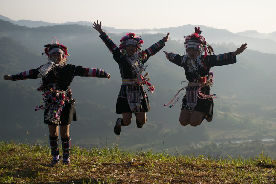 res personas con coloridos trajes tradicionales Akha saltando de alegría en una colina con montañas de fondo